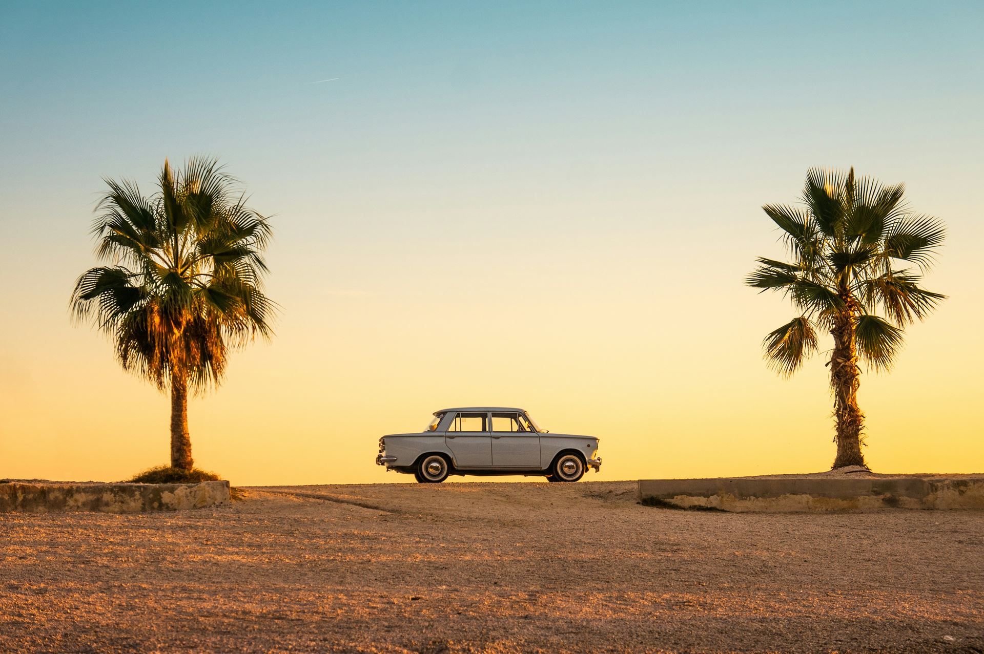 a sunset sceme with two palm trees and a car silhouetted on the horizon